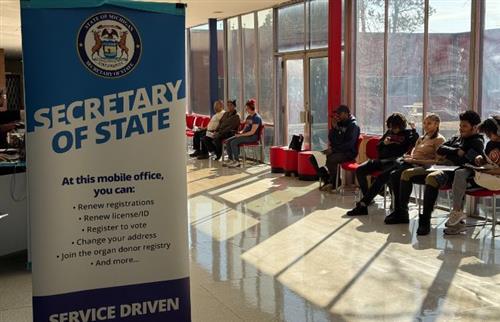 Secretary of State Banner and students sitting in chairs waiting for service
